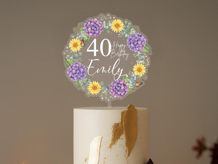 A white cake with a wreath of purple and yellow flowers on top, and the number &quot;40&quot; written on it.