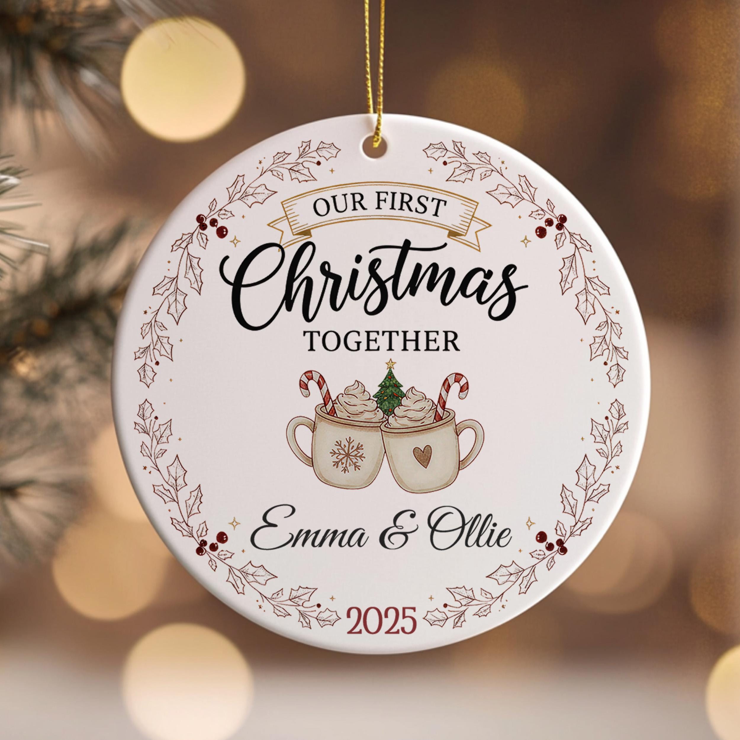 A white Christmas ornament with the text "OUR FIRST CHRISTMAS TOGETHER" and an illustration of two mugs with hot chocolate and candy canes.