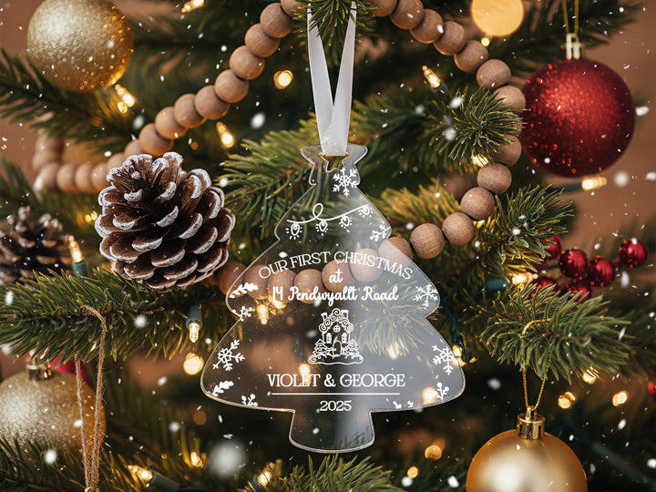 A close-up view of a Christmas tree adorned with ornaments, including a clear ornament shaped like a tree, pine cones, and a red ornament.