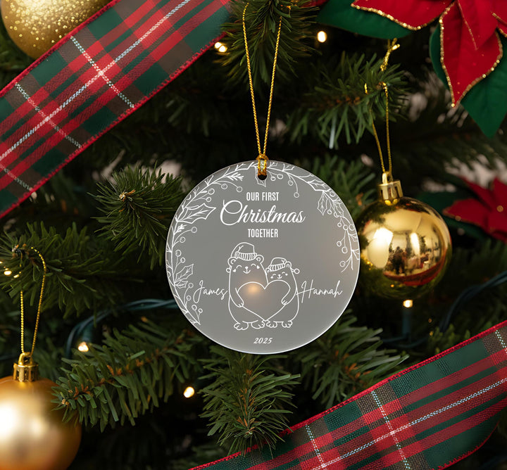 A Christmas tree decorated with ornaments, including a clear ornament with a couple and the text &quot;Our first Christmas together&quot; and &quot;James and Hannah&quot; written on it.