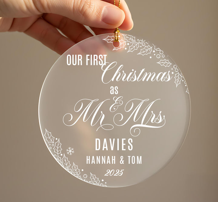 A hand holding a clear ornament with the text &quot;OUR FIRST Christmas as Mr & Mrs DAVIES Hannah & Tom 2025&quot; written on it.