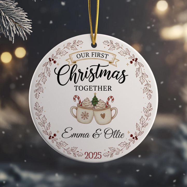 A white Christmas ornament with a gold ribbon, featuring a couple enjoying hot chocolate together.