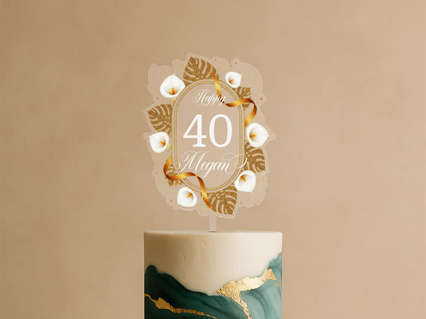 Personalised gold and white acrylic cake topper with calla lilies and ribbon reading “Happy 40 Megan” on green-gold cake