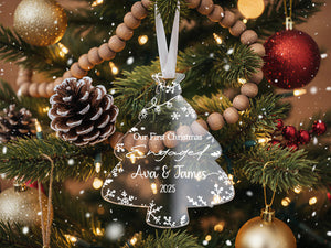 A Christmas tree decorated with ornaments, including a clear ornament that says "Our First Christmas Engaged Ava & James 2020" and a pine cone ornament.