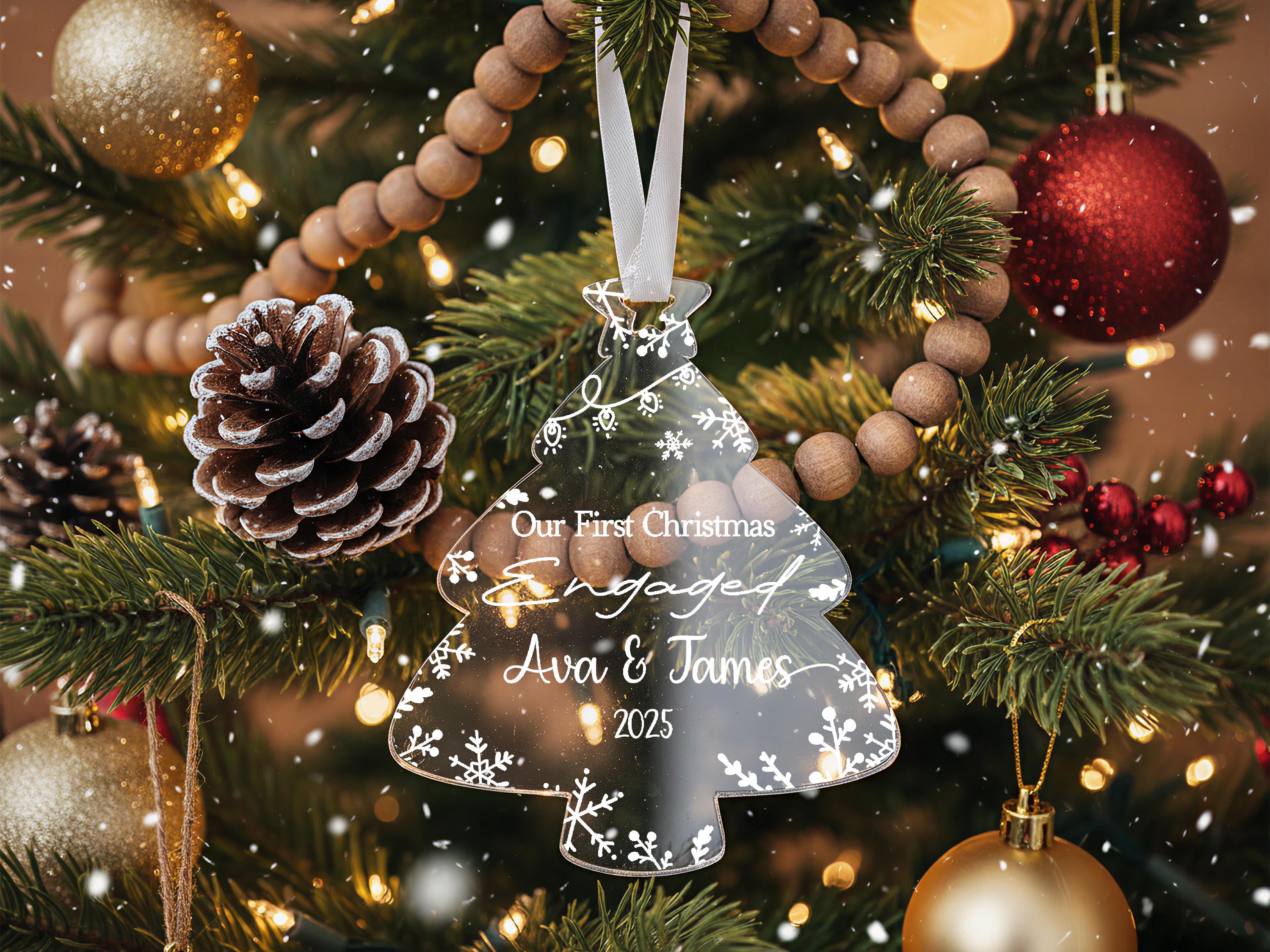 A Christmas tree decorated with ornaments, including a clear ornament that says "Our First Christmas Engaged Ava & James 2020" and a pine cone ornament.