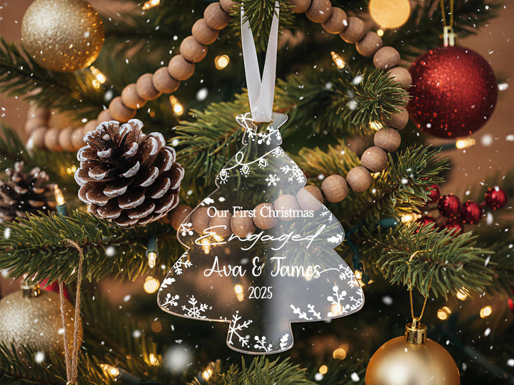 A Christmas tree decorated with ornaments, including a clear ornament that says &quot;Our First Christmas Engaged Ava & James 2020&quot; and a pine cone ornament.