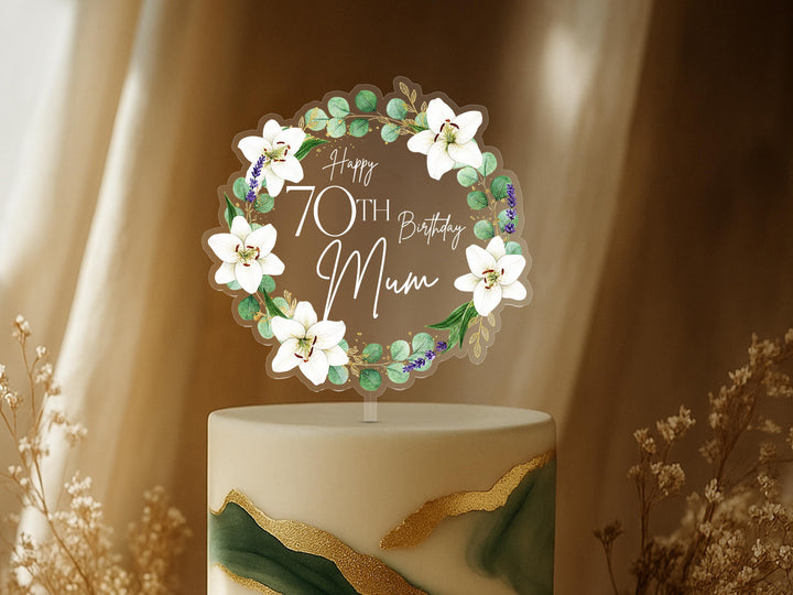 A cake topper with a wreath of white flowers and greenery, celebrating a 70th birthday.