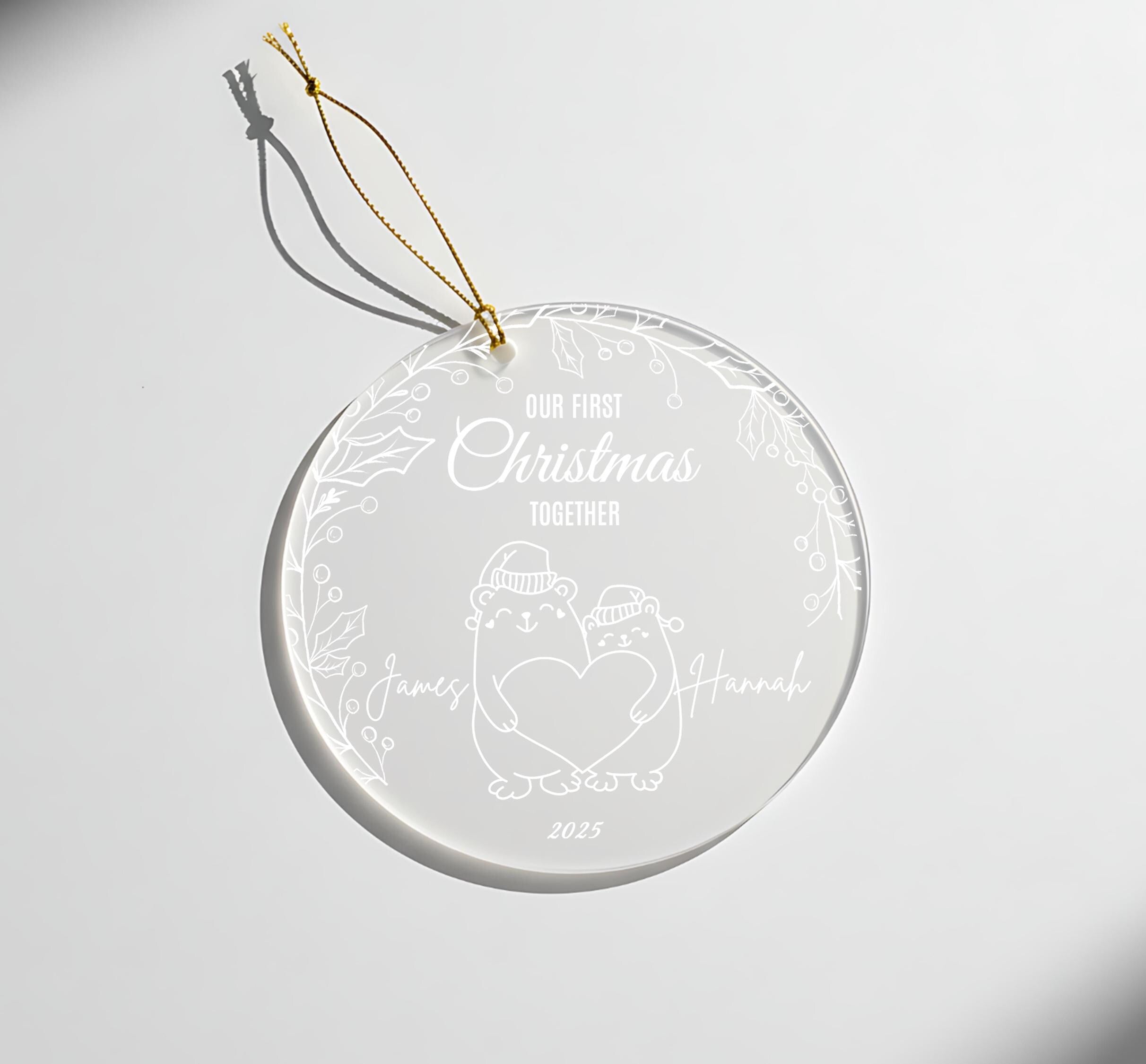 A clear glass ornament with a white design and text, hanging on a white surface.