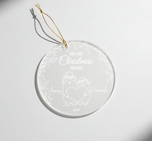 A clear glass ornament with a white design and text, hanging on a white surface.