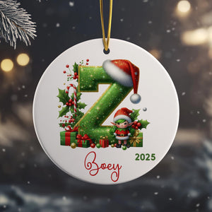 A white ornament with a green number "Z" and a Santa hat, along with a small elf figure, is hanging from a string.
