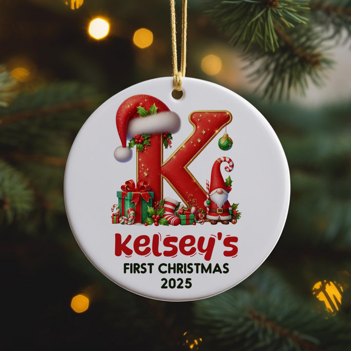 A white ornament with a red letter &quot;K&quot; and various Christmas-themed decorations, including a Santa hat, presents, and a gnome, hanging on a Christmas tree.