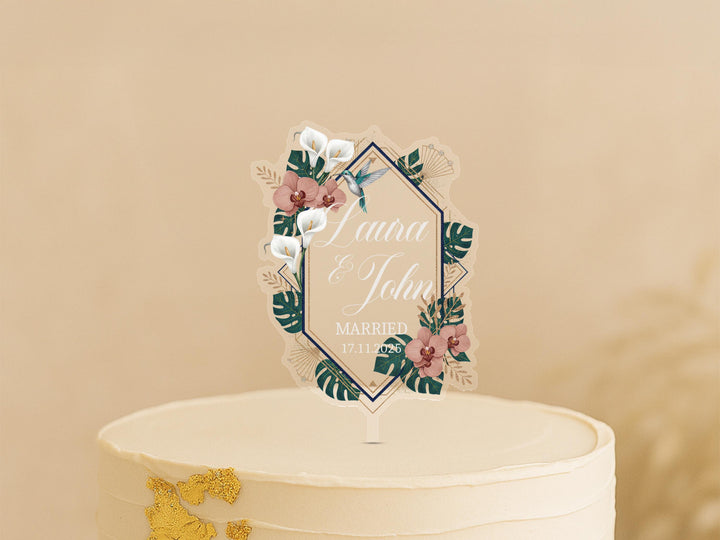 A white wedding cake with a decorative floral topper featuring the names &quot;Lena & John&quot; and the date &quot;MARCH 17, 2020&quot;.