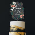 Personalised Art Deco wedding cake topper featuring geometric gold and emerald green frame with white calla lilies, terracotta orchids, tropical palm leaves and hummingbird, custom names Laura and John, Married 17.11.2025, displayed on elegant gold and black painted cake