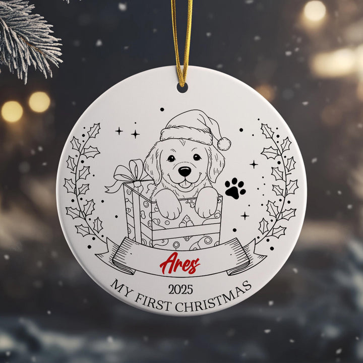 A white ornament with a black and white illustration of a dog wearing a Santa hat, holding a gift box, and surrounded by holly leaves and a ribbon.