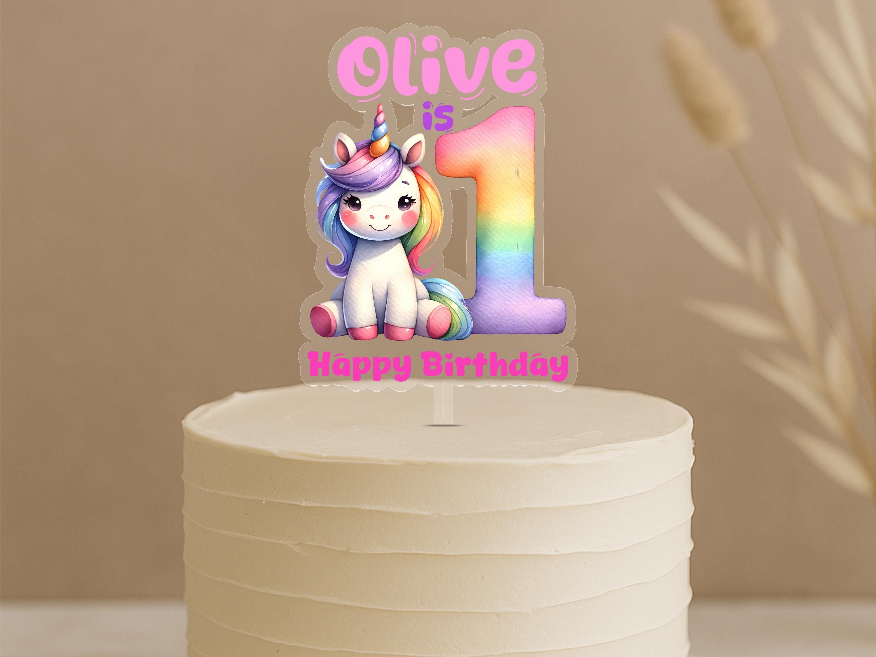 Personalised unicorn first birthday cake topper showing rainbow number 1 with cute unicorn and custom name Olive on white celebration cake
