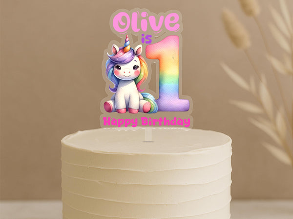 Personalised unicorn first birthday cake topper showing rainbow number 1 with cute unicorn and custom name Olive on white celebration cake
