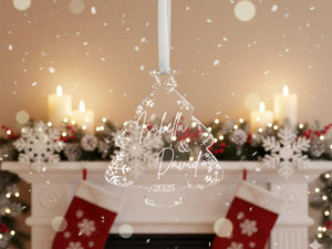 A Christmas ornament with the names "Isabella & David" and the year "2025" is hanging in front of a fireplace decorated with snowflakes and candles.