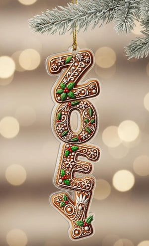 A gingerbread house ornament in the shape of the name "Zoey" is hanging from a branch of a Christmas tree.