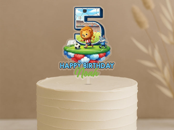 A birthday cake with a number 5 topper featuring a cartoon lion and soccer player.