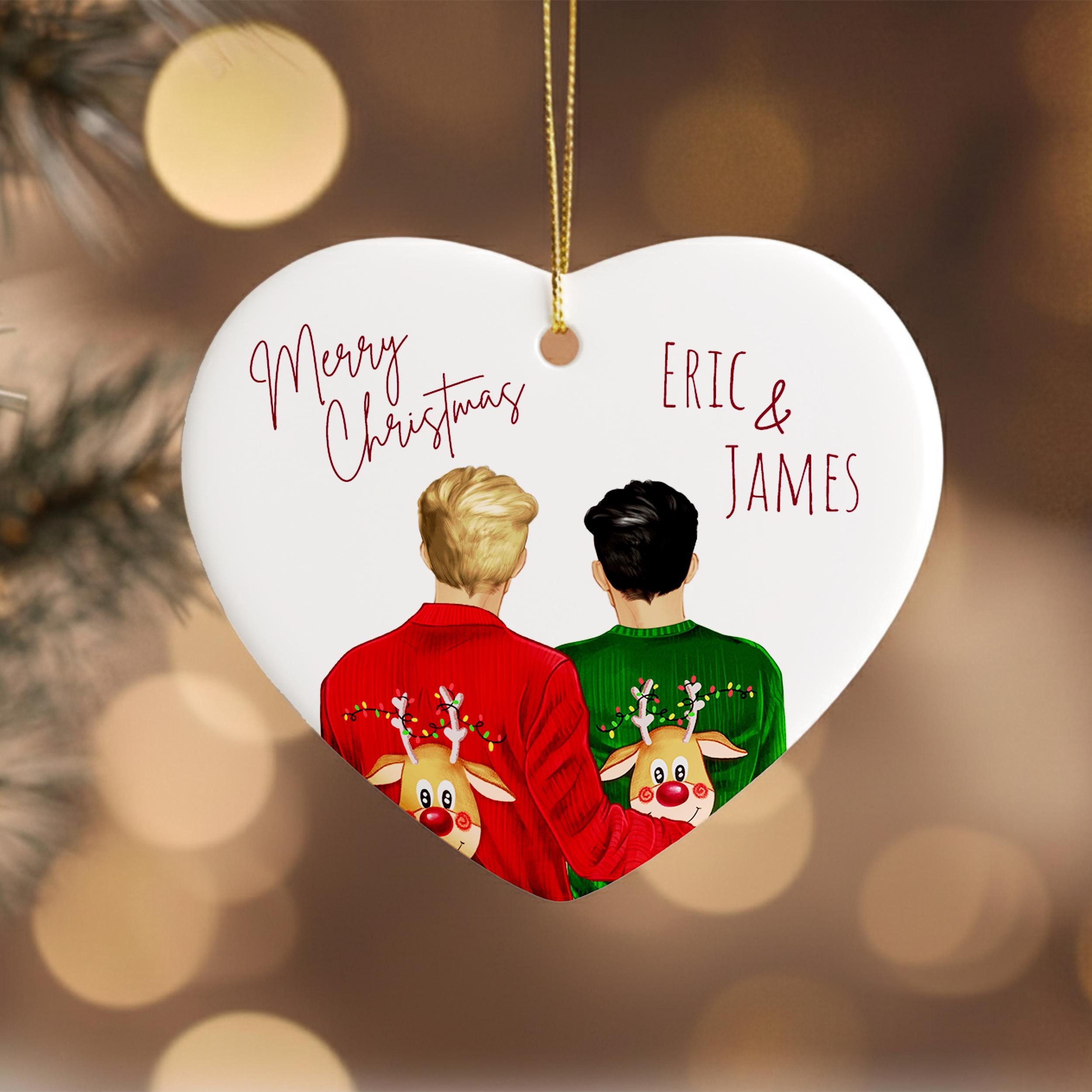 A heart-shaped ornament with two people wearing Christmas sweaters, one red and one green, with a string of lights in the background.