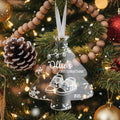 A Christmas tree decorated with ornaments, including a clear ornament shaped like a baby's foot, surrounded by pine cones, red and gold ornaments, and twinkling lights.