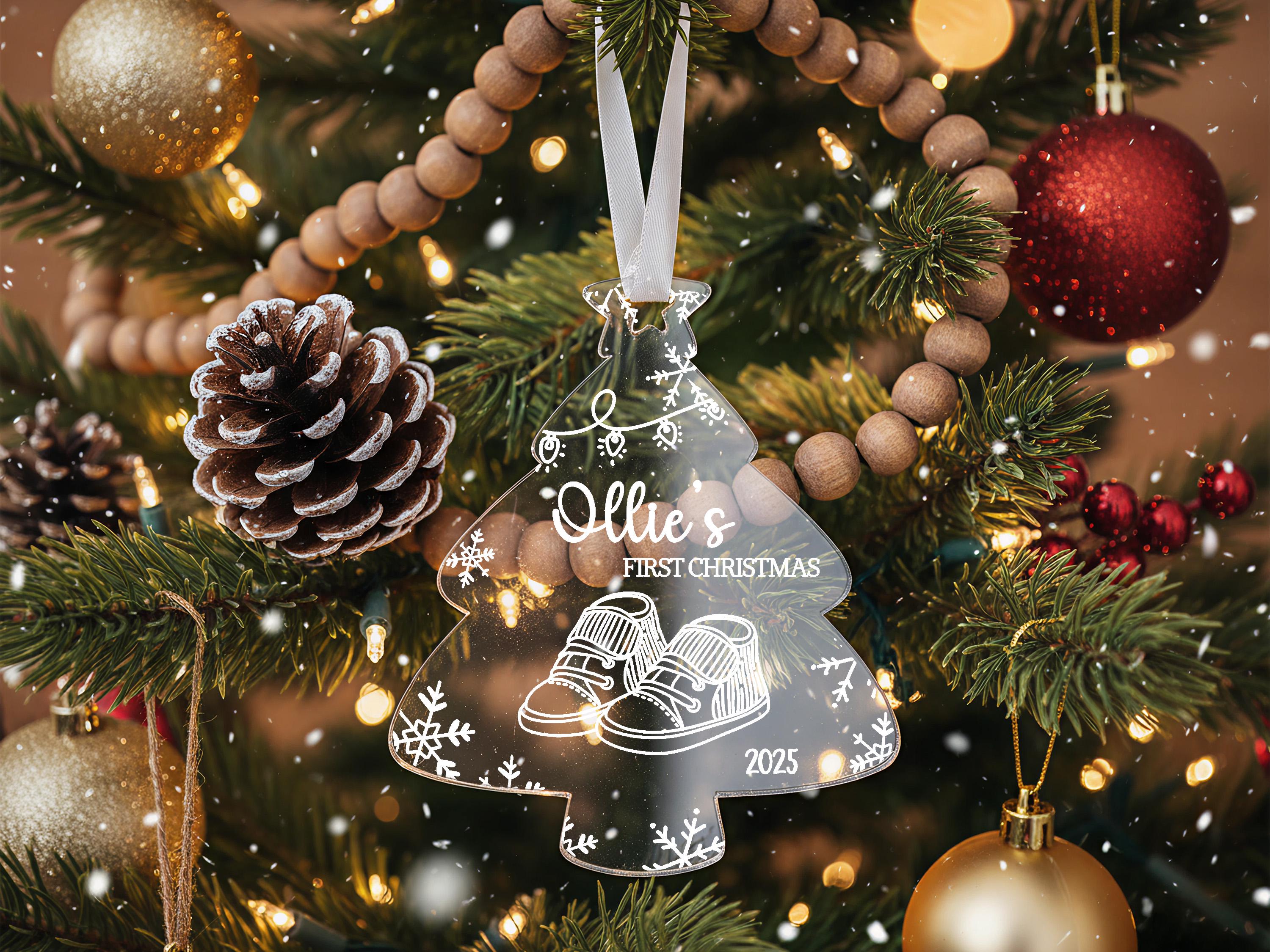 A Christmas tree decorated with ornaments, including a clear ornament shaped like a baby's foot, surrounded by pine cones, red and gold ornaments, and twinkling lights.