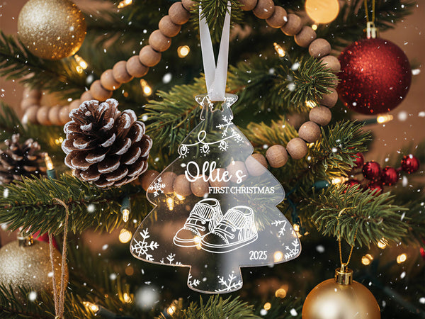 A Christmas tree decorated with ornaments, including a clear ornament shaped like a baby&#39;s foot, surrounded by pine cones, red and gold ornaments, and twinkling lights.