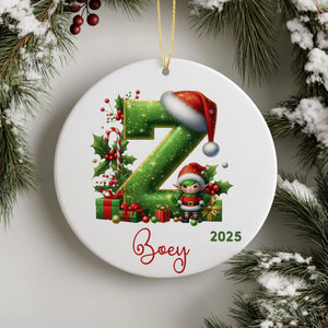 A white ornament with a green letter "Z" and a small elf wearing a Santa hat, surrounded by Christmas decorations such as presents and holly leaves.