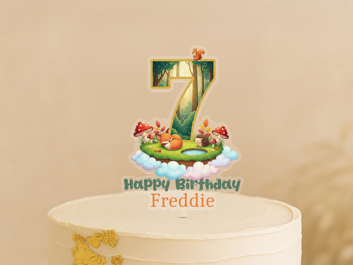 Woodland animal cake topper showing number 7 with forest creatures, trees and mushrooms on magical woodland landscape, personalised with name Freddie, displayed on white birthday cake
