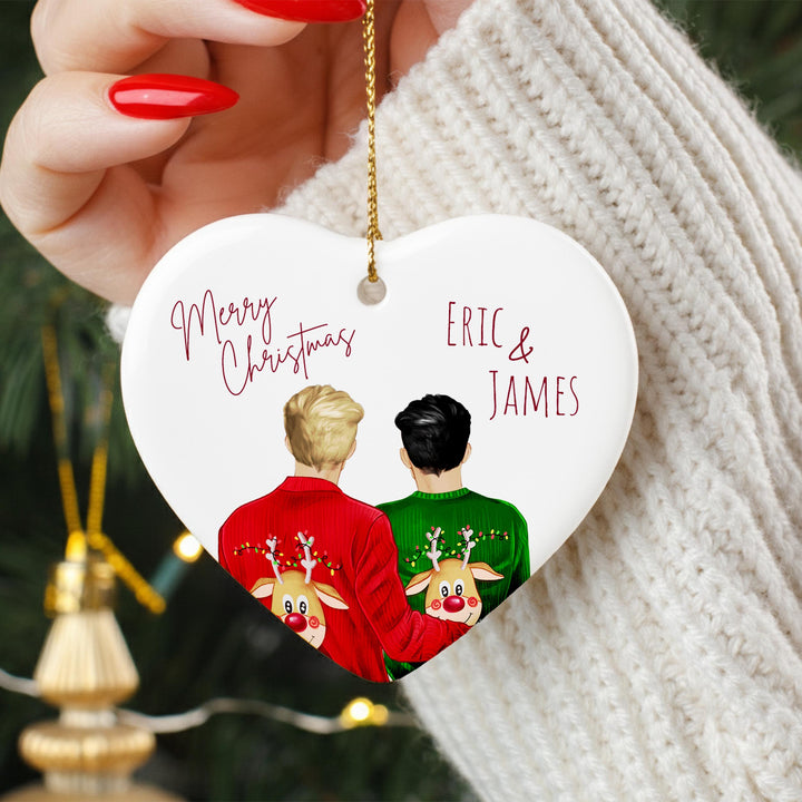 A heart-shaped ornament with two people wearing Christmas sweaters, one in red and the other in green, with the text &quot;Merry Christmas Eric & James&quot; on it.