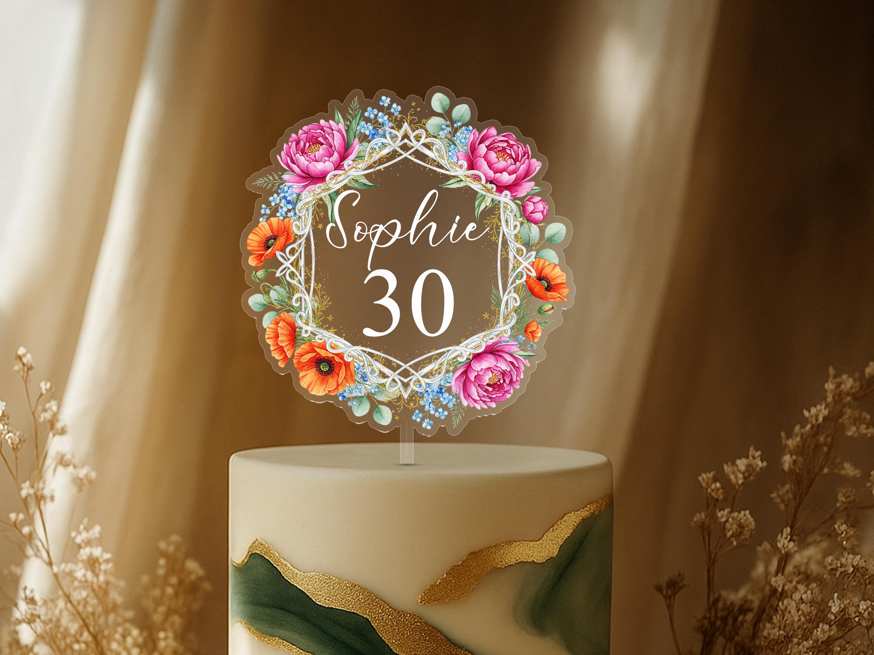 A cake topper with a floral design and the name "Sophie" written on it, placed on top of a cake.