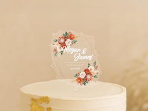 A white wedding cake with a clear floral topper displaying the names "Megan & James" and the date "23/03/2023".