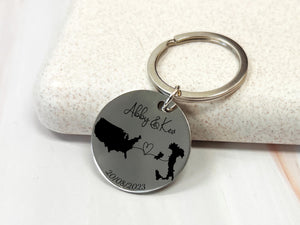 Personalised country map keychain with two engraved countries, names, connecting heart, and date, custom long distance relationship gift.