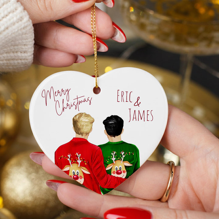 A heart-shaped ornament with two people wearing Christmas sweaters and reindeer on their backs, holding the ornament in their hands.