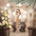 A gingerbread house ornament with the name "ALEX" made of gingerbread pieces is hanging from a branch.