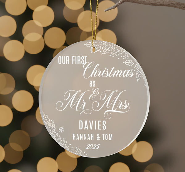 Personalised first Christmas as Mr and Mrs frosted acrylic ornament hanging with gold ribbon showing elegant engraved text Our First Christmas as Mr & Mrs, surname Davies, names Hannah and Tom 2025, decorated with holly leaves, berries and snowflakes against bokeh lightsRetry