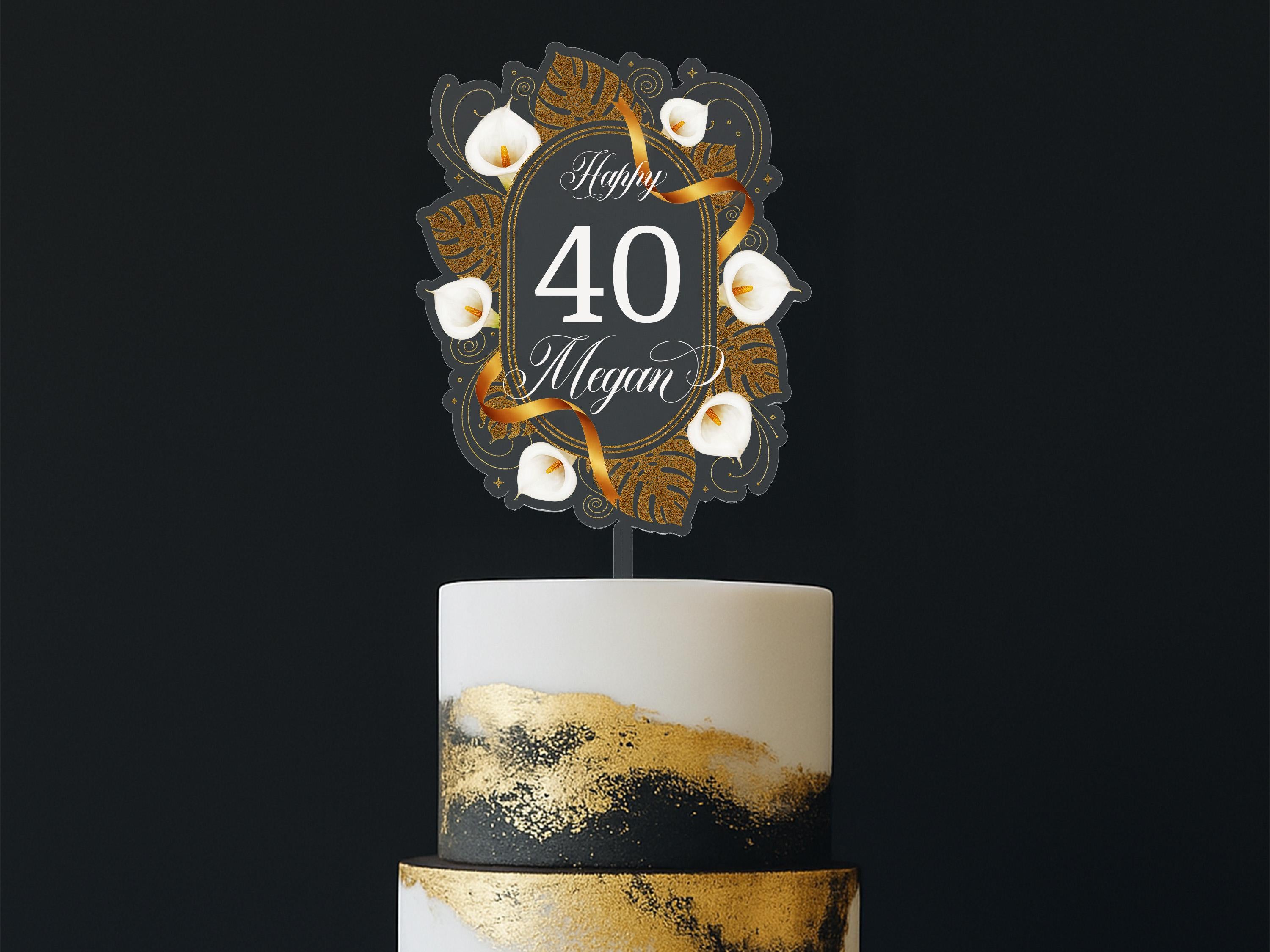 A white cake with gold and black designs, and a decorative topper that says "Happy 40 Megan" in a gold and black design.