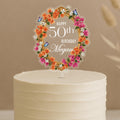 Personalised 50th birthday cake topper featuring elegant floral wreath with orange and pink flowers, butterflies and custom name Megan on white celebration cake