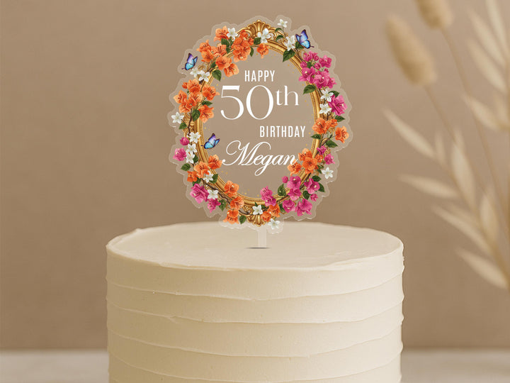 Personalised 50th birthday cake topper featuring elegant floral wreath with orange and pink flowers, butterflies and custom name Megan on white celebration cake