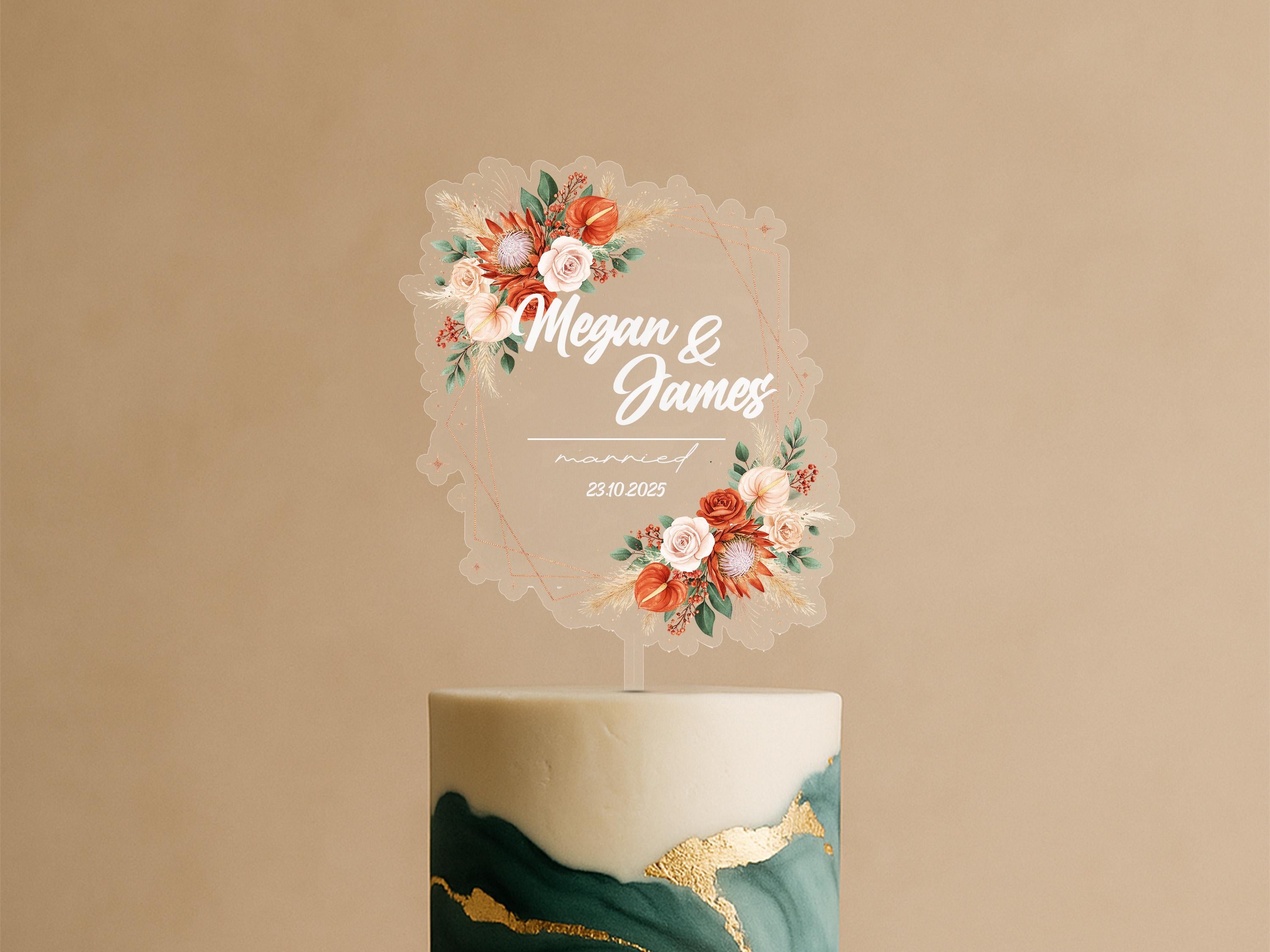 A wedding cake topper with the names 'Megan & James' and the date '23.10.2021' displayed on it, surrounded by a floral design.