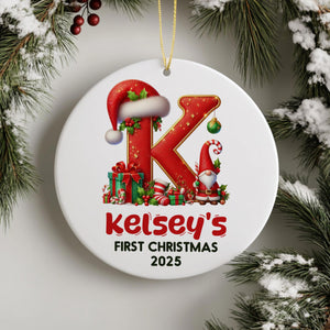 A white Christmas ornament with a red and gold design featuring a letter "K" and a gnome, surrounded by Christmas decorations such as pine branches and berries.
