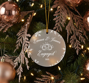 A clear ornament with a white design hangs on a Christmas tree, surrounded by pine branches and ornaments.
