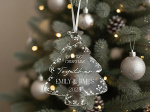A clear Christmas ornament hanging on a tree, featuring the names "Emilly & James" and the year "2025" along with the phrase "Our first Christmas together".