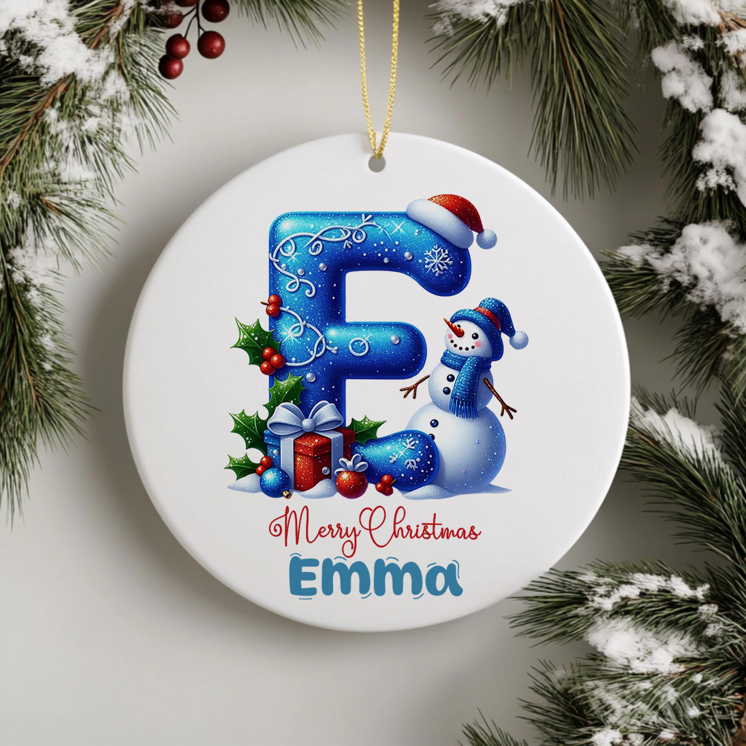 A white ceramic ornament with a snowman and Christmas decorations, including a red bow, holly leaves, and a gift box, hanging on a string.