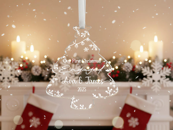 Personalised clear acrylic Christmas tree ornament engraved with Our First Christmas Engaged, names Ava & James 2025, featuring snowflakes and botanical details, hanging on Christmas tree with festive decorations