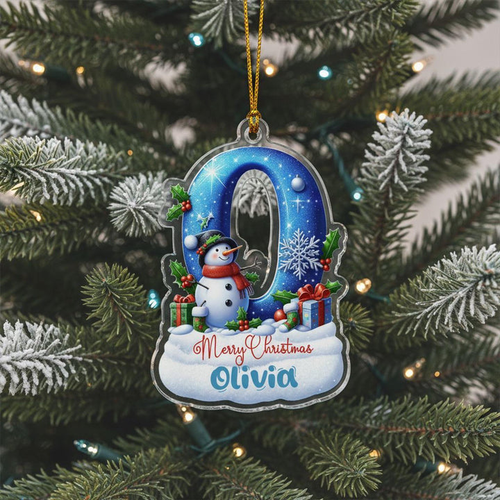 A Christmas ornament shaped like the number 0, featuring a snowman and other winter-themed decorations, is hanging on a pine tree.