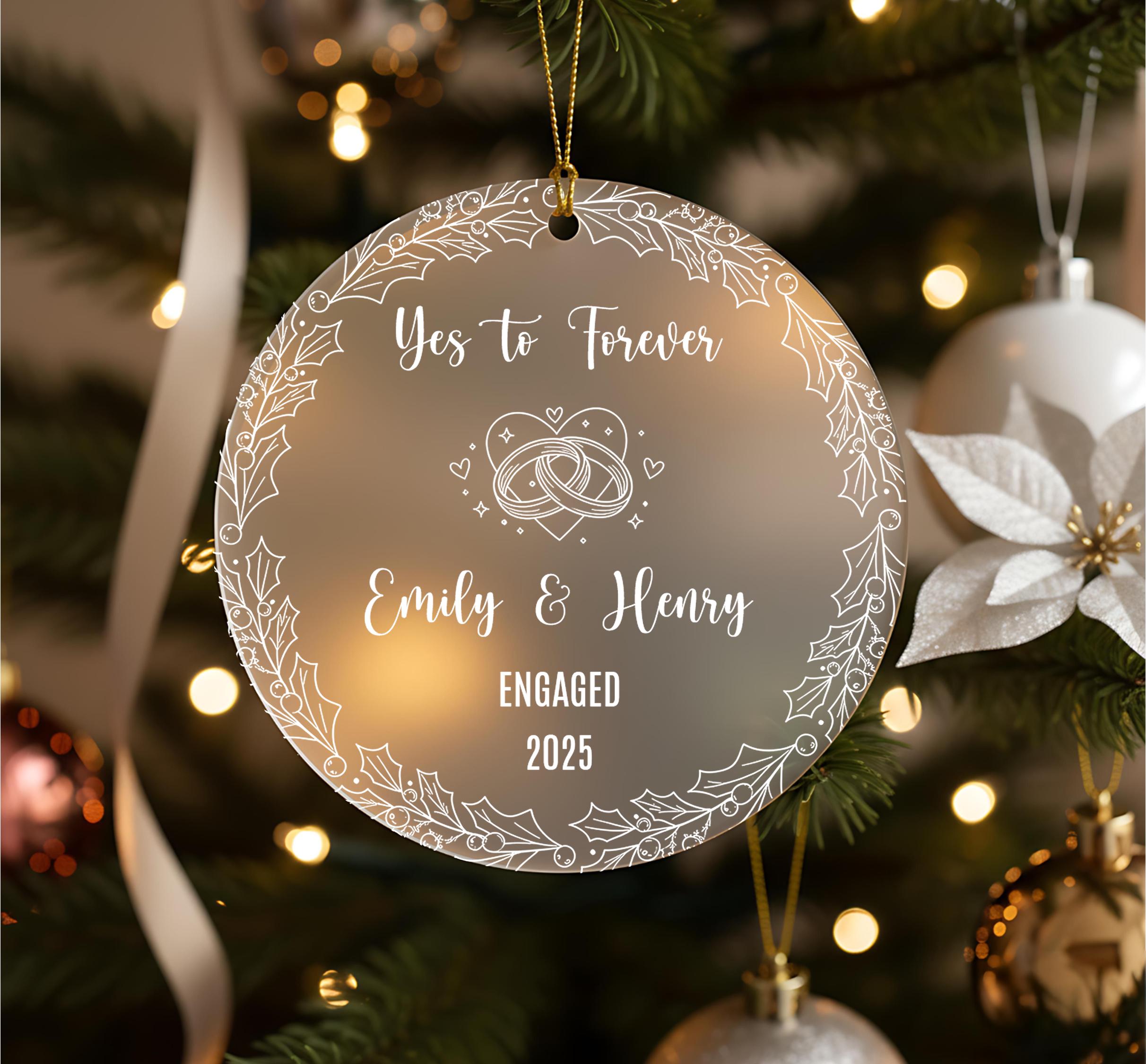 A round ornament hanging on a Christmas tree, with the text "Yes to Forever Emily & Henry Engaged 2020" written on it.