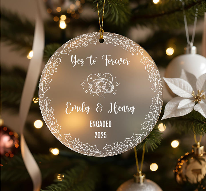 A round ornament hanging on a Christmas tree, with the text &quot;Yes to Forever Emily & Henry Engaged 2020&quot; written on it.