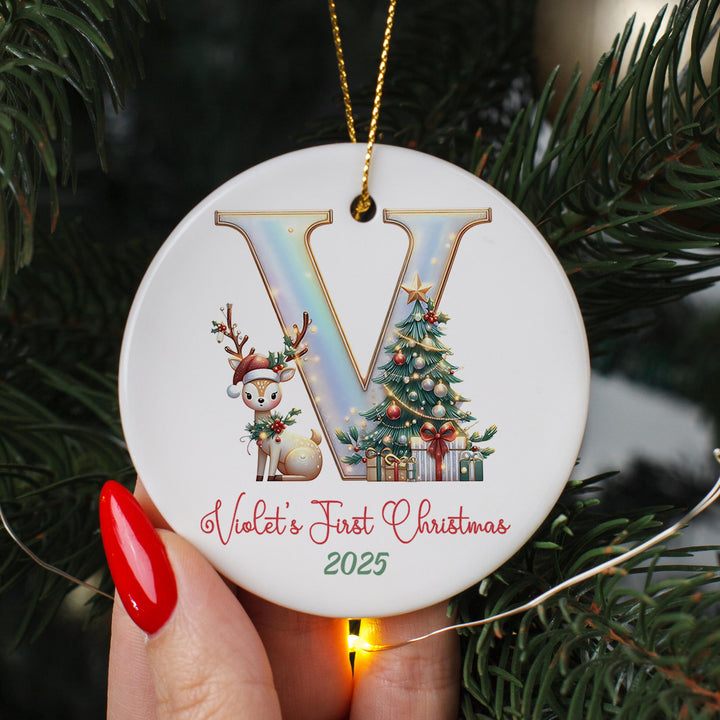 A person&#39;s hand holding a decorative ornament with a letter &#39;V&#39; and a Christmas tree design.