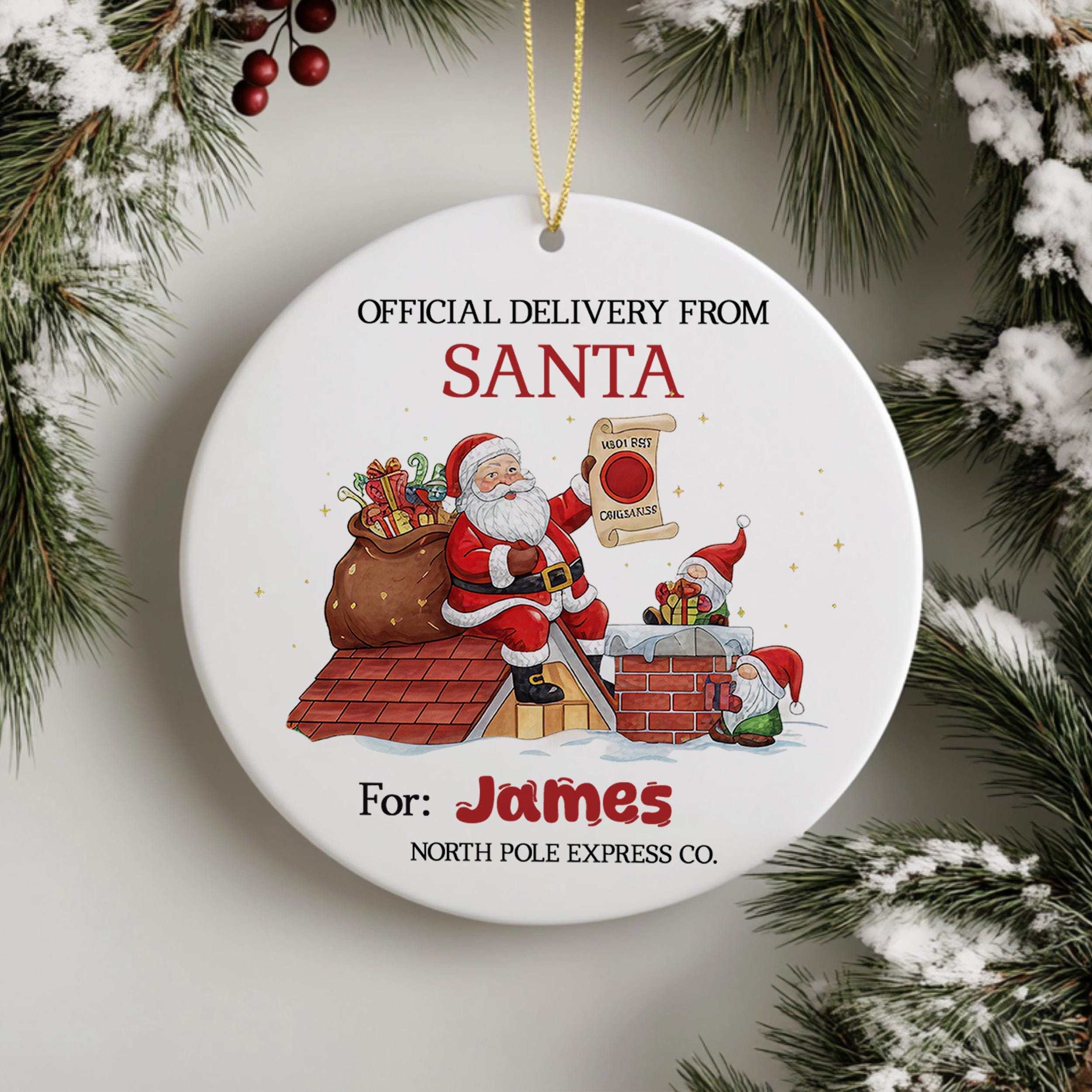 a Christmas ornament with a Santa Claus figure holding a bag of presents, standing on a rooftop with a chimney. The ornament is labeled as an "Official Delivery from Santa" and is intended for a person named James.